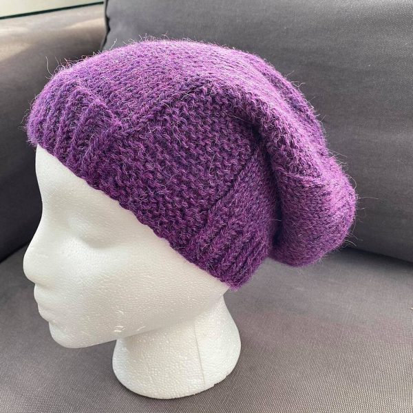 a slouchy hat knit in purple yarn with garter stitch columns up each side on a foam head