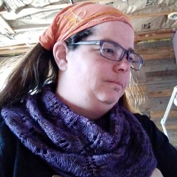 A model wearing a cowl in purple yarn with diamond shaped lace leaves and a wide garter stitch border