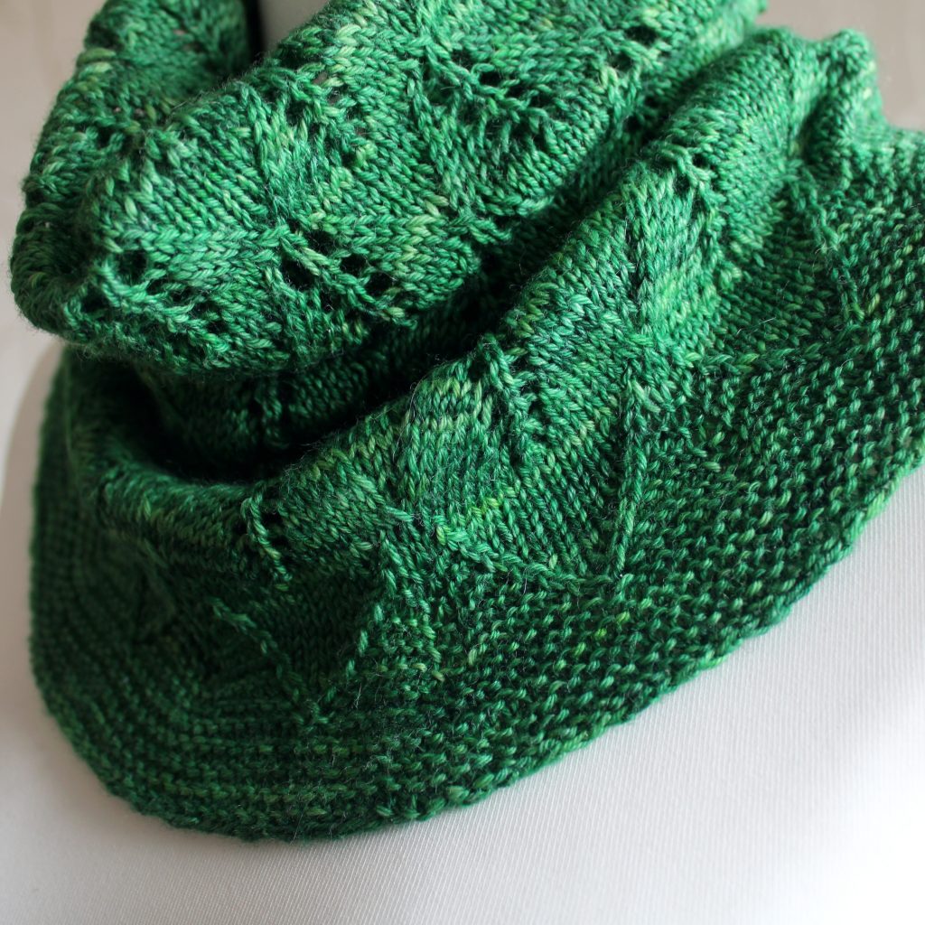 A close up on a green cowl with diamond shaped leaves and a wide lace border modelled on a mannequin