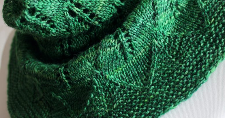 A close up on a green cowl with diamond shaped leaves and a wide lace border modelled on a mannequin