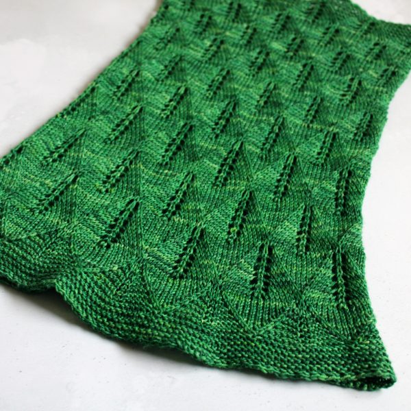 A green cowl with diamond shaped lace leaves and wide garter stitch borders laid flat to show the tapered shape and the increasing leaf size from top to bottom