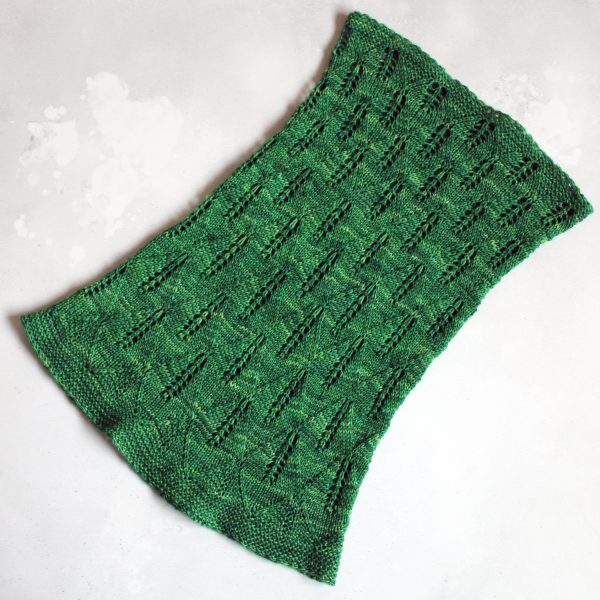 A green cowl with diamond shaped lace leaves and wide garter stitch borders laid flat to show the tapered shape and the increasing leaf size from top to bottom