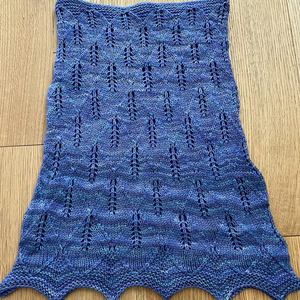 A blue coloured cowl with diamond shaped lace leaves and wide garter stitch borders laid flat