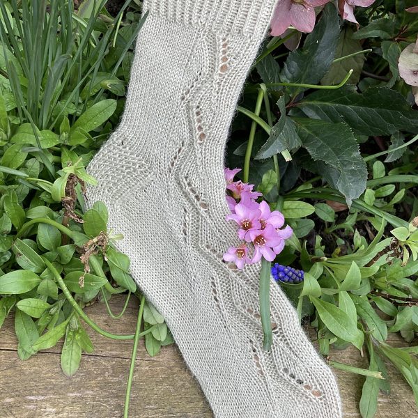 A sock handknit in pale green yarn on a sock blocker to show the zigzag lace pattern up the outside of the foot and leg