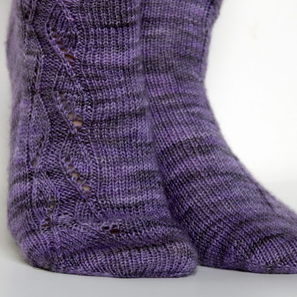 A close up on the toes of a purple pair of socks with a zigzagging lace pattern up the outside of each foot