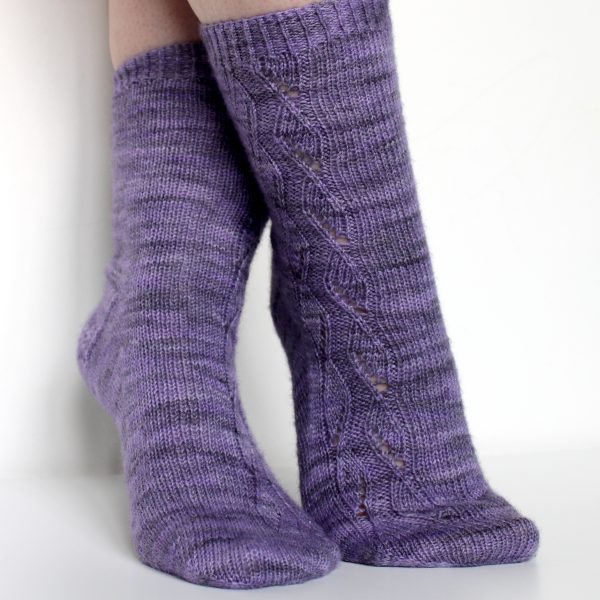 A pair of socks handknit in purple yarn showing the zigzag lace pattern up the outside of one foot and leg, and showing the gusset and textured heel pattern on the other foot