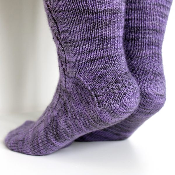 A pair of socks handknit in purple yarn showing textured heel pattern on both socks