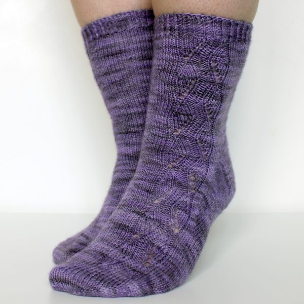 A pair of socks handknit in purple yarn showing the zigzag lace pattern up the outside of one foot and leg,