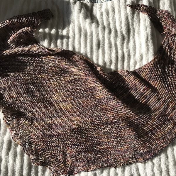 A brown shawl with a diamond edge and a rippled border laid on a blanket