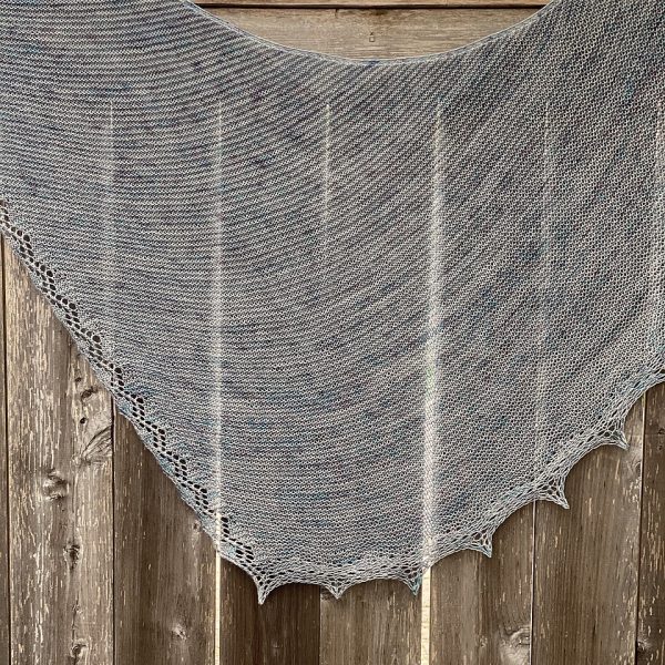 A silvery grey shawl with a diamond edge and a rippled border over a fence