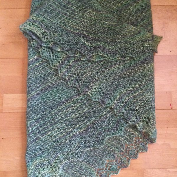 A green variegated shawl with a diamond edge and a rippled border folded on a wooden background