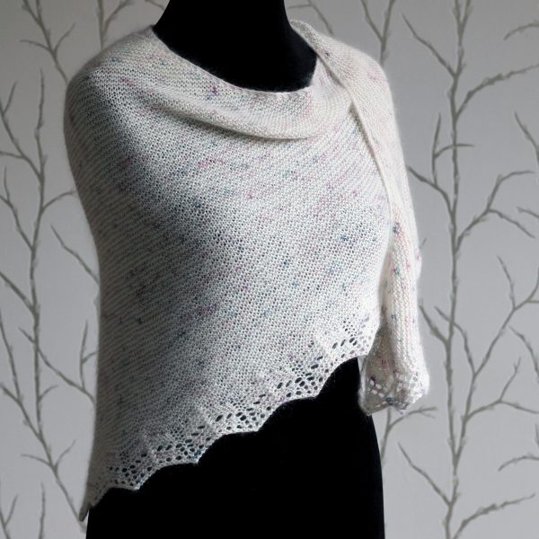 A white speckled shawl with a rippling lace pattern along the edge modelled on a mannequin