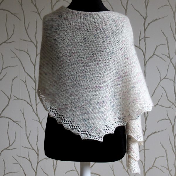 A white speckled shawl with a diamond lace pattern along one edge and a rippled border on the other draped over a mannequin