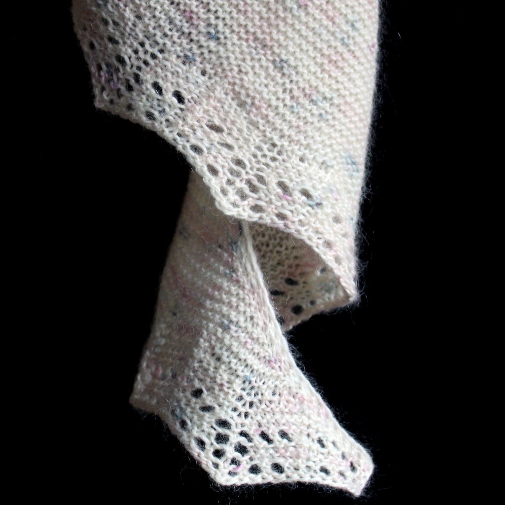 The corner of a shawl hanging down in a spiral showing the garter stitch lace edge