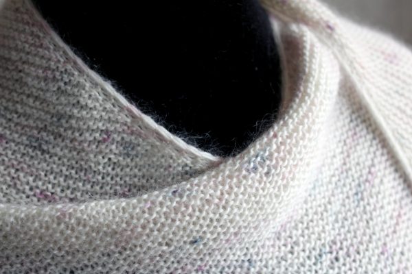 A white speckled shawl wrapped around a mannequin showing the softness of the yarn and garter stitch