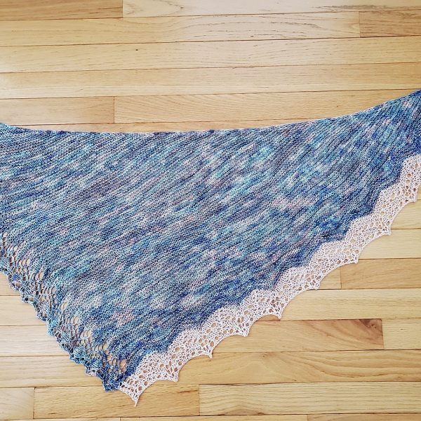 A variegated shawl with a diamond edge and a contrast rippled border on a wooden background