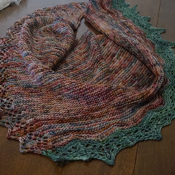 A variegated shawl with a diamond edge and a contrast rippled border on a wooden background