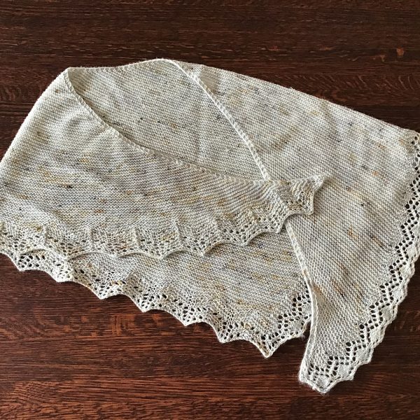 A speckled cream shawl with a diamond edge and a rippled border folded on a wooden background