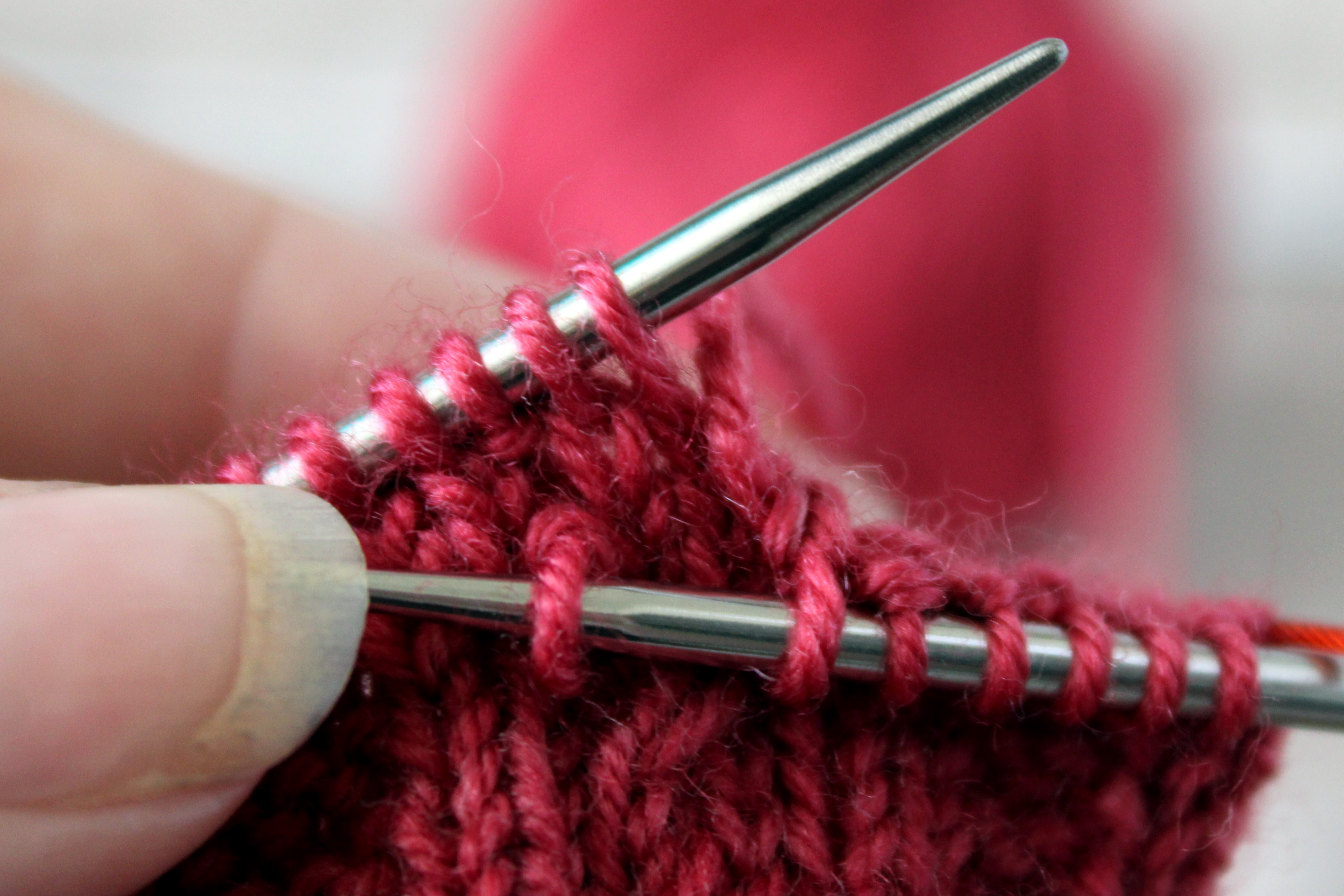 The right hand needle is inserted into the stitch hanging at the front of your knitting