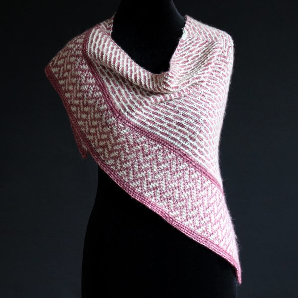 A mosaic knit shawl knit in white and red yarn with a brickwork pattern on the body and herringbone pattern border, displayed on a black mannequin.