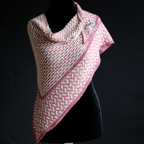 A mosaic knit shawl knit in white and red yarn with a brickwork pattern on the body and herringbone pattern border, displayed on a black mannequin.