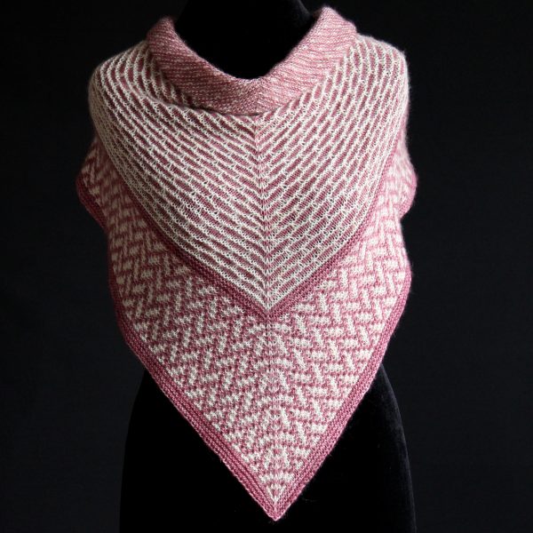 A mosaic knit shawl knit in white and red yarn with a brickwork pattern on the body and herringbone pattern border, displayed on a black mannequin.