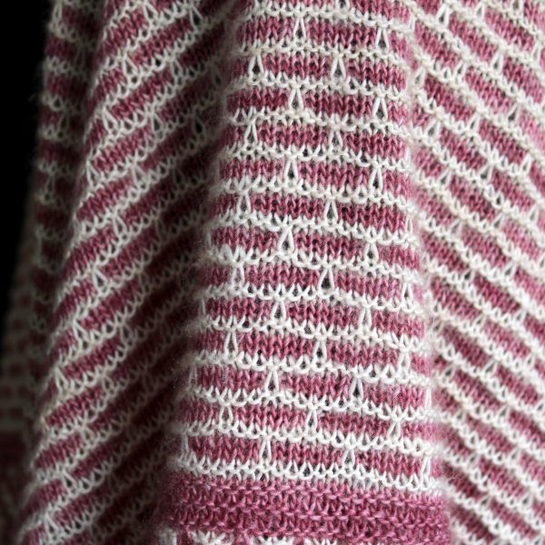 A close up on the body of a mosaic knit shawl. It is knit in white and red yarn with a brickwork pattern on the body