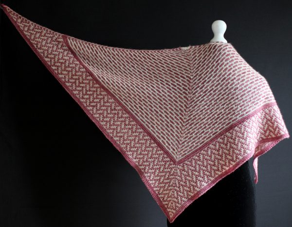 A mosaic knit shawl knit in white and red yarn with a brickwork pattern on the body and herringbone pattern border. The shawl is spread out to show the triangular shape