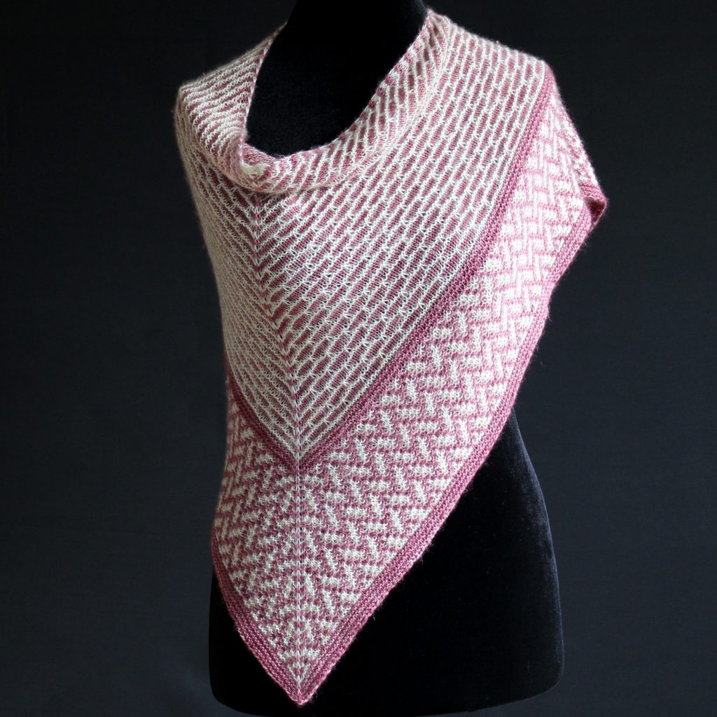 A mosaic knit shawl knit in white and red yarn with a brickwork pattern on the body and herringbone pattern border, displayed on a black mannequin.