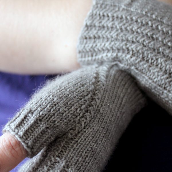 Two fingerless mitts with a twisted rib cuff and a textured rib pattern up both sides and around the thumb, knitted in grey yarn.