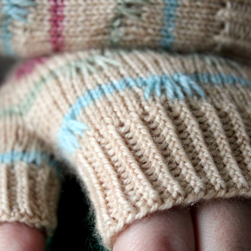 A close up on the twisted rib cuff of a pair of mitts with coloured stripes and slipped stitches