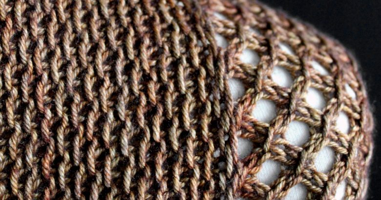 A close up on the shoulder of a cowlette knit in brown yarn with a textured slipped stitch pattern on the body and a wide lace border