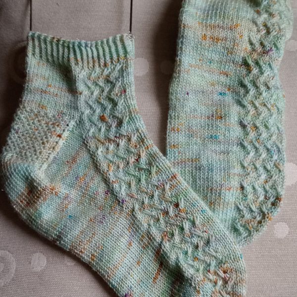 A pair of socks with a rippling cable pattern up the side, knit in mint speckled yarn