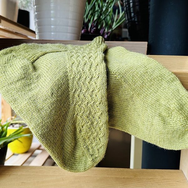 A pair of socks with a rippling cable pattern up the side, knit in light green yarn