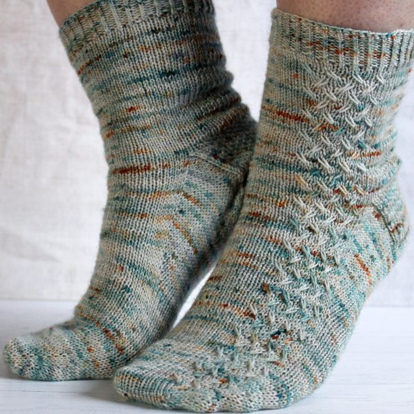 A modelled pair of socks with a rippling cable pattern up the side, knit in grey yarn with blue, orange and white speckles