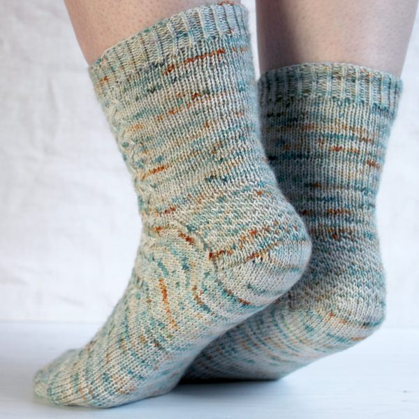 A modelled pair of socks with a rippling cable pattern up the side, showing the textured heel pattern, knit in grey yarn with blue, orange and white speckles