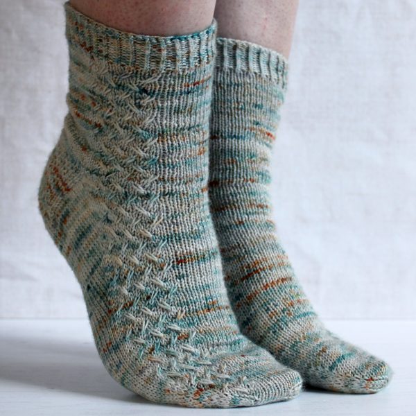 A modelled pair of socks with a rippling cable pattern up the side, knit in grey yarn with blue, orange and white speckles