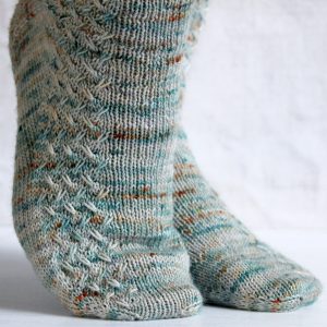 A modelled pair of socks with a rippling cable pattern up the side, knit in grey yarn with blue, orange and white speckles