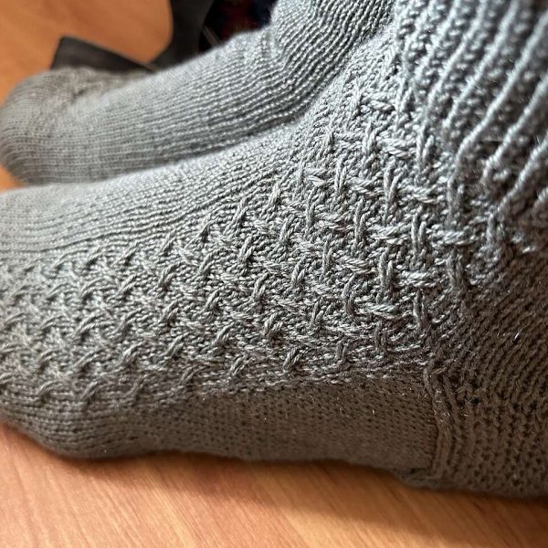 A modelled pair of socks with a rippling cable pattern up the side, knit in grey yarn