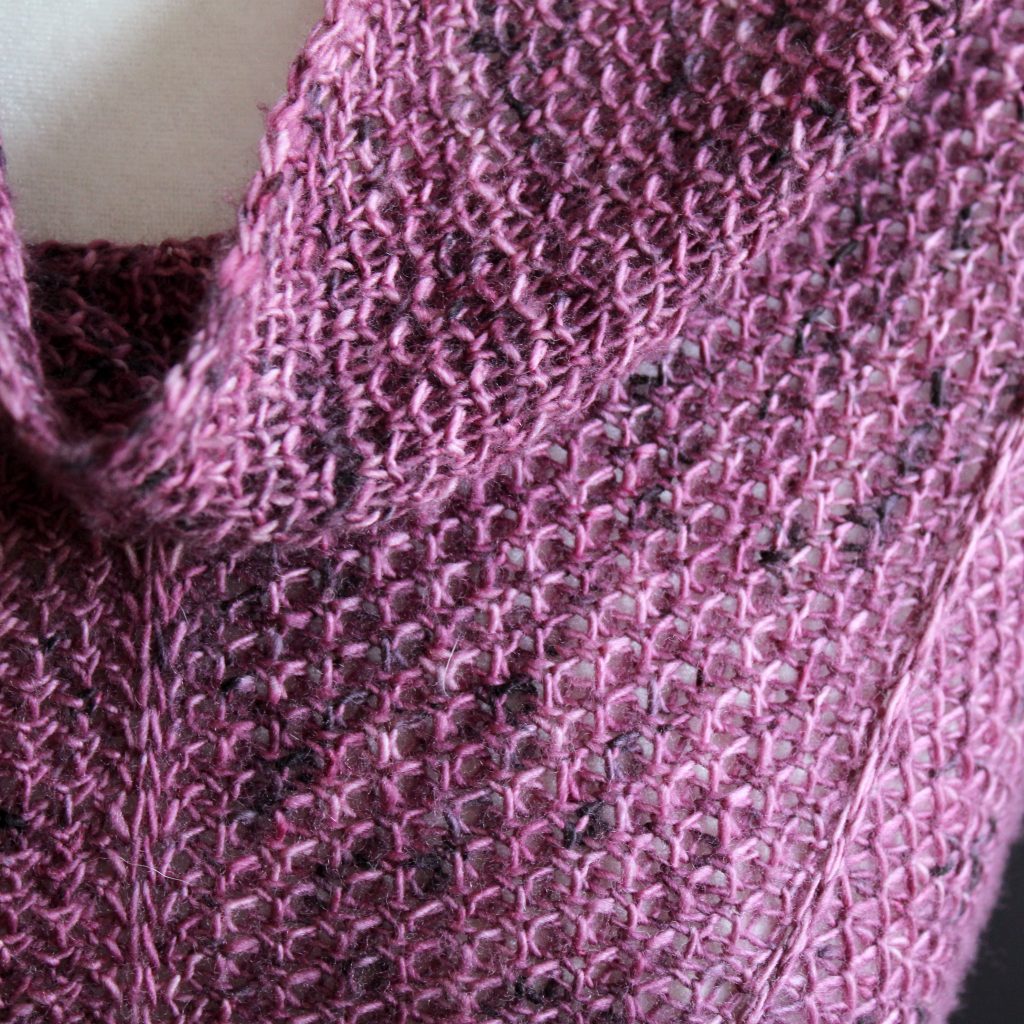 A close up on the spine and border of a cowlette knit in purple yarn with two brioche patterns and two slipped stitch bands