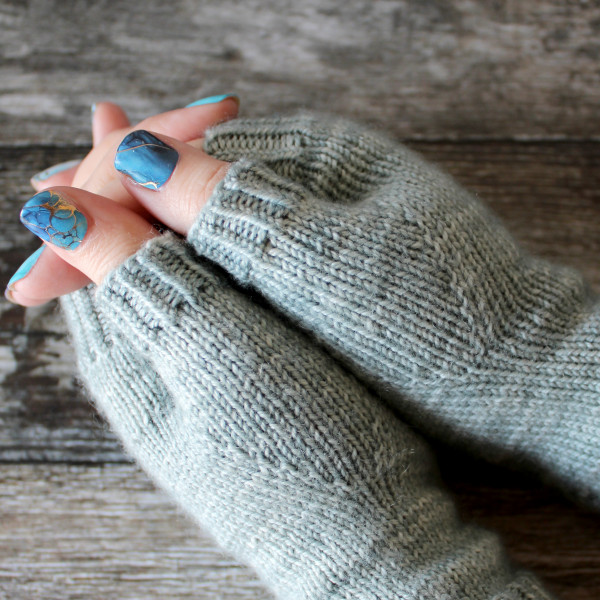 A close up on the thumbs of a pair of fingerless mitts knit in a pale blue yarn