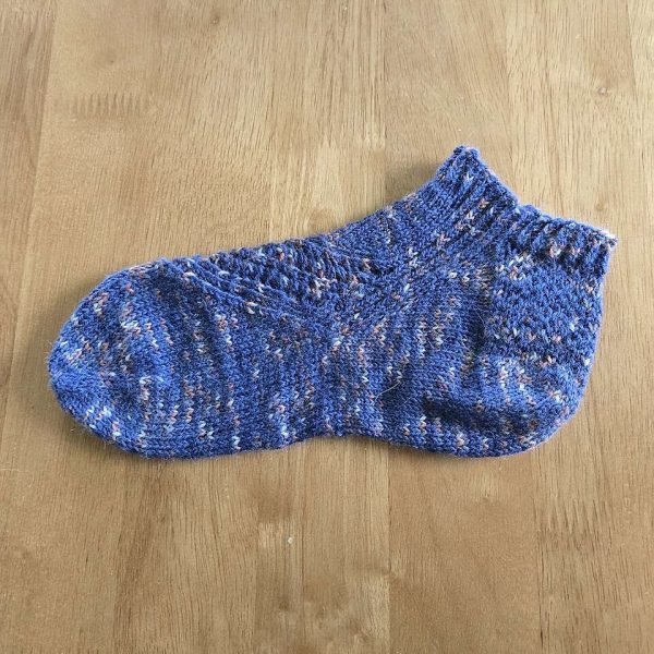 A trainer sock with a lace and twisted rib pattern travelling across the sock. The socks are knit in a blue yarn with speckles.