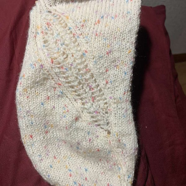 A trainer sock with a lace and twisted rib pattern travelling across the sock. The socks are knit in a white yarn with speckles.