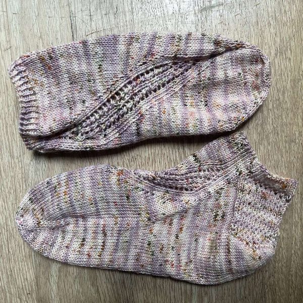 A pair of trainer socks with a lace and twisted rib pattern travelling across the sock. The socks are knit in grey yarn with speckles.