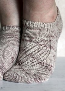 Trainer socks with a lace and twisted rib pattern travelling across the sock. The socks are knit in light brown yarn with speckles.