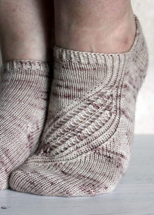 Trainer socks with a lace and twisted rib pattern travelling across the sock. The socks are knit in light brown yarn with speckles.