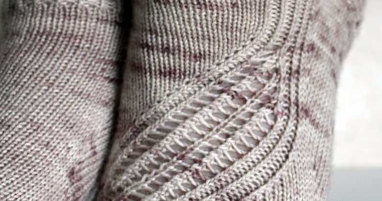 Trainer socks with a lace and twisted rib pattern travelling across the sock. The socks are knit in light brown yarn with speckles.