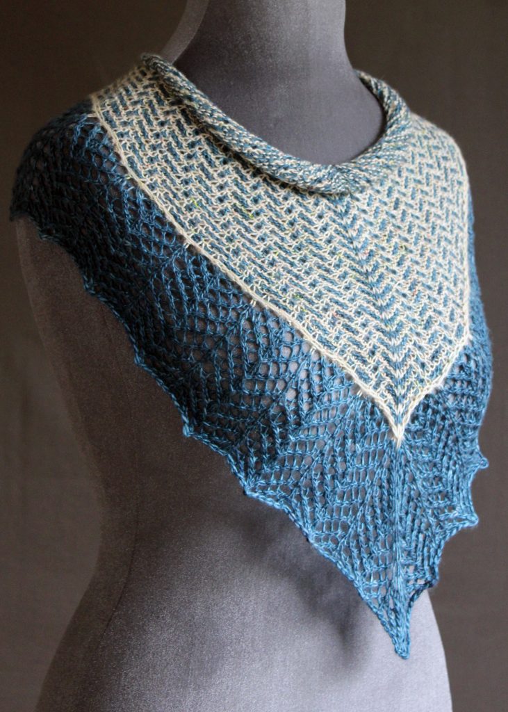 A cowlette with a mosaic body, knit in blue and white yarn, with a wide lace border knit in blue.