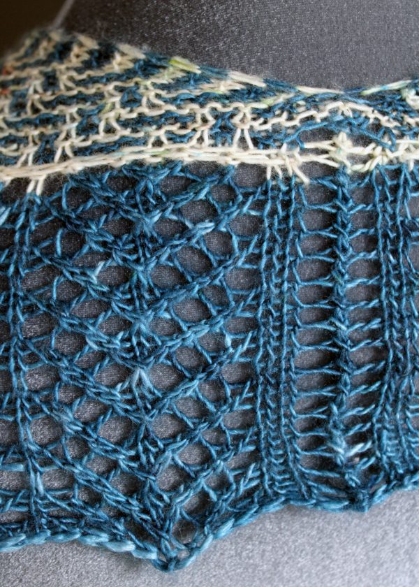 The back of a cowlette with a mosaic body, knit in blue and white yarn, with a wide lace border knit in blue.