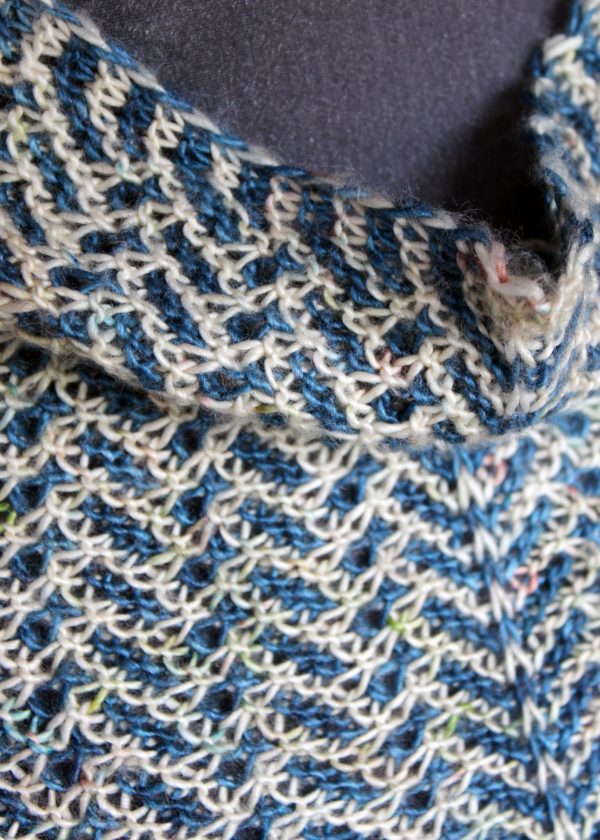 A close up on a cowlette with a mosaic body, knit in blue and white yarn.
